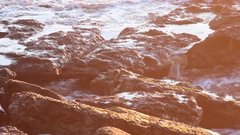 Vista-Cinematográfica-Entre-Rocas-Y-Piedras,-El-Sol-Se-Refleja-En-El-Agua-Del-Océano,-Secuencia-De-Video-En-Cámara-Lenta-Que-Captura-Momentos-En-La-Naturaleza