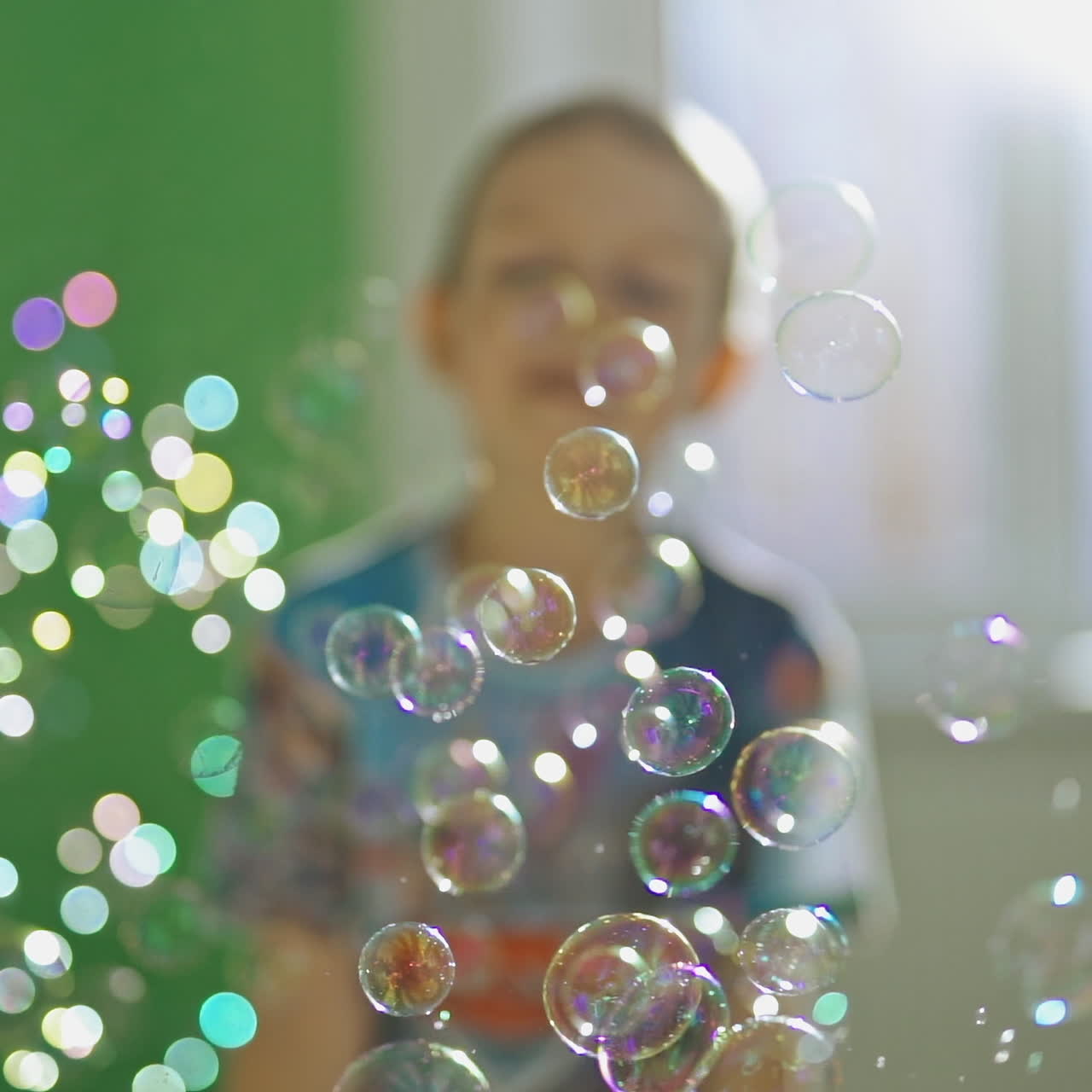Colorful bubbles flying in the room on blurred background. Many soap bubbles and a boy catching them indoors. Close-up.