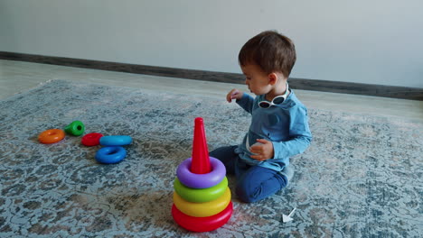caucasian child playing with toy pyramid at home. kid sits on the floor collecting rings on the base.