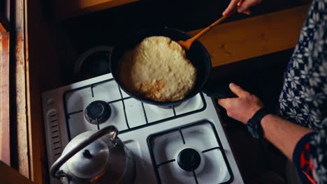 a person is flipping a pancake in a pan inside a rustic kitchen at reinsjøen, åfjord, trøndelag, norway - high angle shot