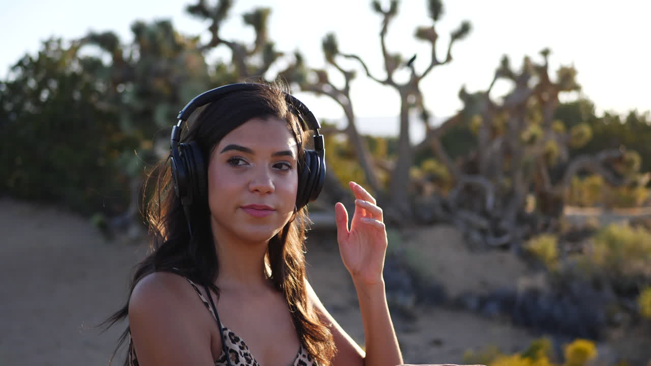A beautiful young woman listening to music on her headphones outdoors in nature SLOW MOTION