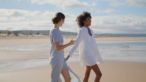 Alegre-Pareja-De-Lesbianas-Caminando-Por-La-Orilla-Del-Mar-En-Video-Vertical.-Chicas-Felices-Se-Toman-De-La-Mano