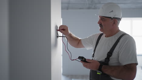 un hombre electricista comprueba el voltaje en la red con un probador de cables preparándose para instalar un hogar inteligente. inspección de todos los sistemas por un electricista profesional