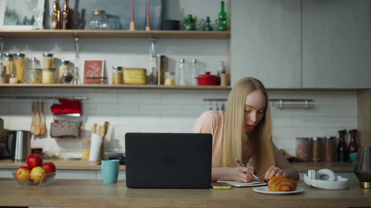 estudiante estudiando en línea sentada en la cocina con una computadora portátil. mujer tomando notas.