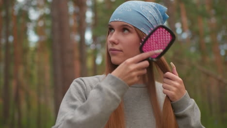 young woman with blue bandana brushes her long hair in peaceful forest setting, enjoying tranquil moment, natural beauty and relaxation in serene outdoor environment surrounded by trees