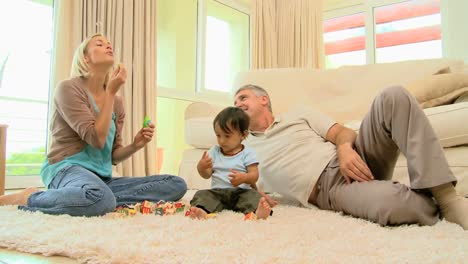 Mother-blowing-bubbles-for-baby-and-husband-on-carpet