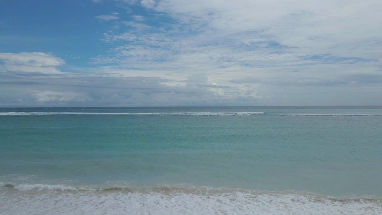 Una serena scena di spiaggia tropicale con ombrelloni bianchi chiusi su una spiaggia sabbiosa con onde oceaniche turchesi sotto un cielo blu nuvoloso