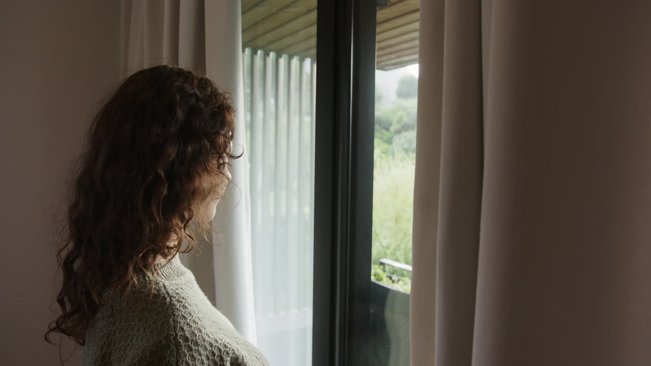 Relaxing at home, woman with curly hair looking out window, enjoying view