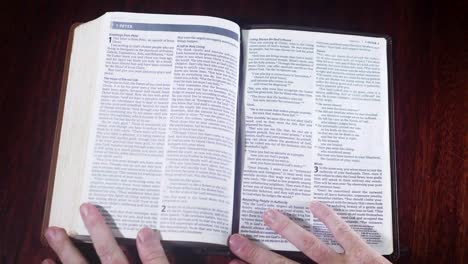 Top-down-shot-of-a-leather-bound-bible-being-opened-up-to-the-book-of-1st-Peter-on-a-wooden-table