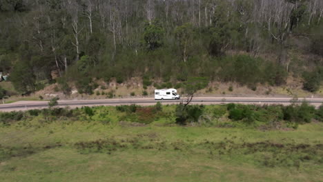 aerial tracking shot of driving campervan on empty scenic road, near mallacoota, australia - holiday trip in woodland of australia