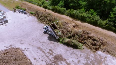 refuse truck is unloading organic vegetation compost garbage on concrete surface, drone aerial view during sunshine day, waste and recycling concept