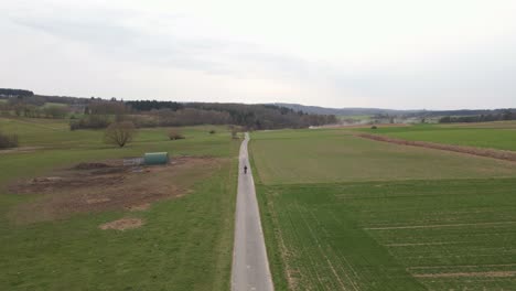 Motorcycle-rider-driving-along-a-straight-and-narrow-countryside-road-in-between-expansive-green-meadows