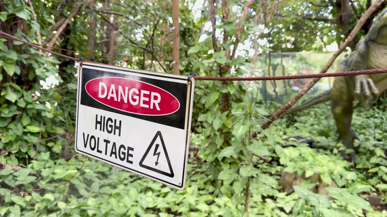Animatronic dinosaur walks behind warning sign in lush, sunlit Australian forest, handheld camera movement