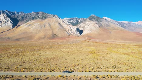 aerial of a 4wd wheel drive vehicle on a road in front of the eastern sierras with mt whitney in ther distance suggesting remote road trip adventure