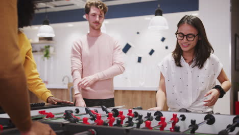 young business creatives relax playing table football at work, one scores a goal, close up