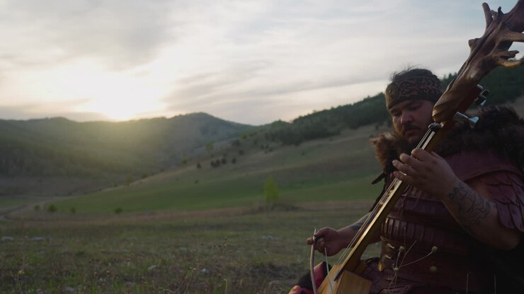 Large man in shaman costume plays ikili sitting in valley