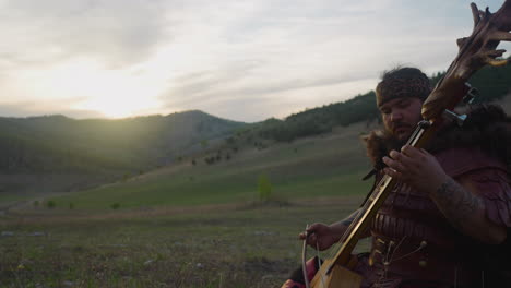 large man in shaman costume plays ikili sitting in valley