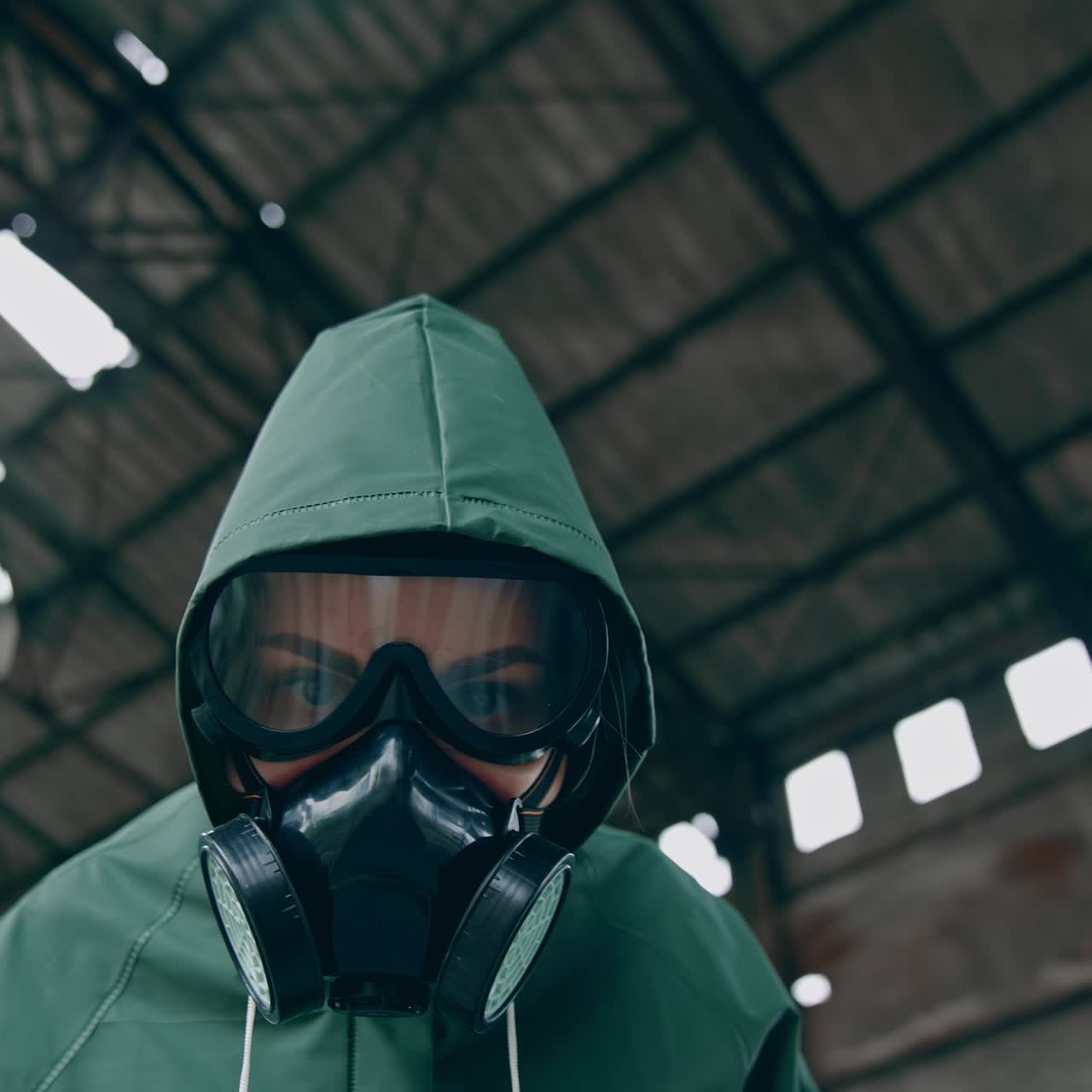 Person in safety chemical suit looks at camera. Portrait of a human in gas mask on ruined building background. View from below. Polluted zone. High level of radiation