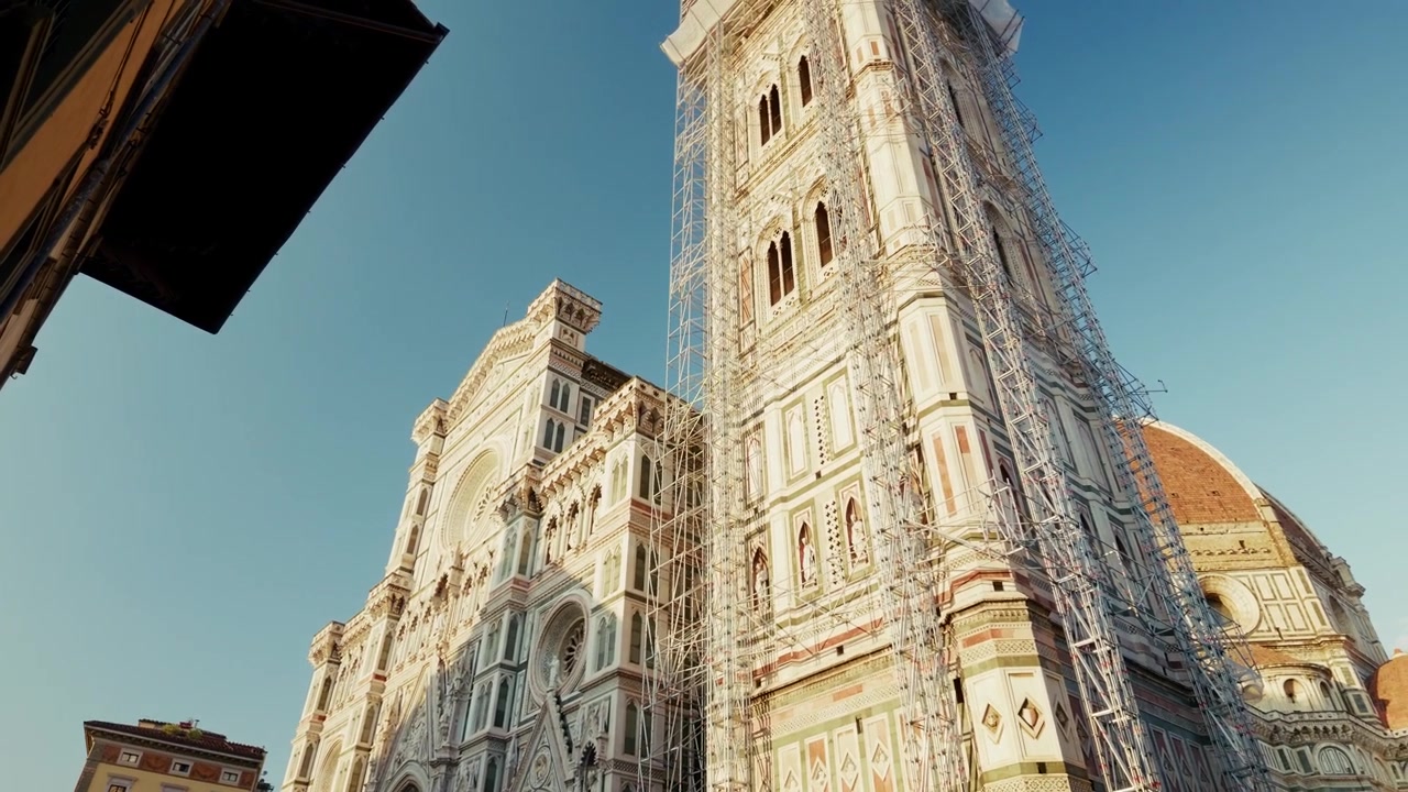 Il campanile di Giotto è avvolto da impalcature di restauro accanto alla cupola in terracotta del Duomo di Firenze, visto da uno stretto vicolo in Toscana. Inquadratura dal basso verso l'alto da uno stretto vicolo