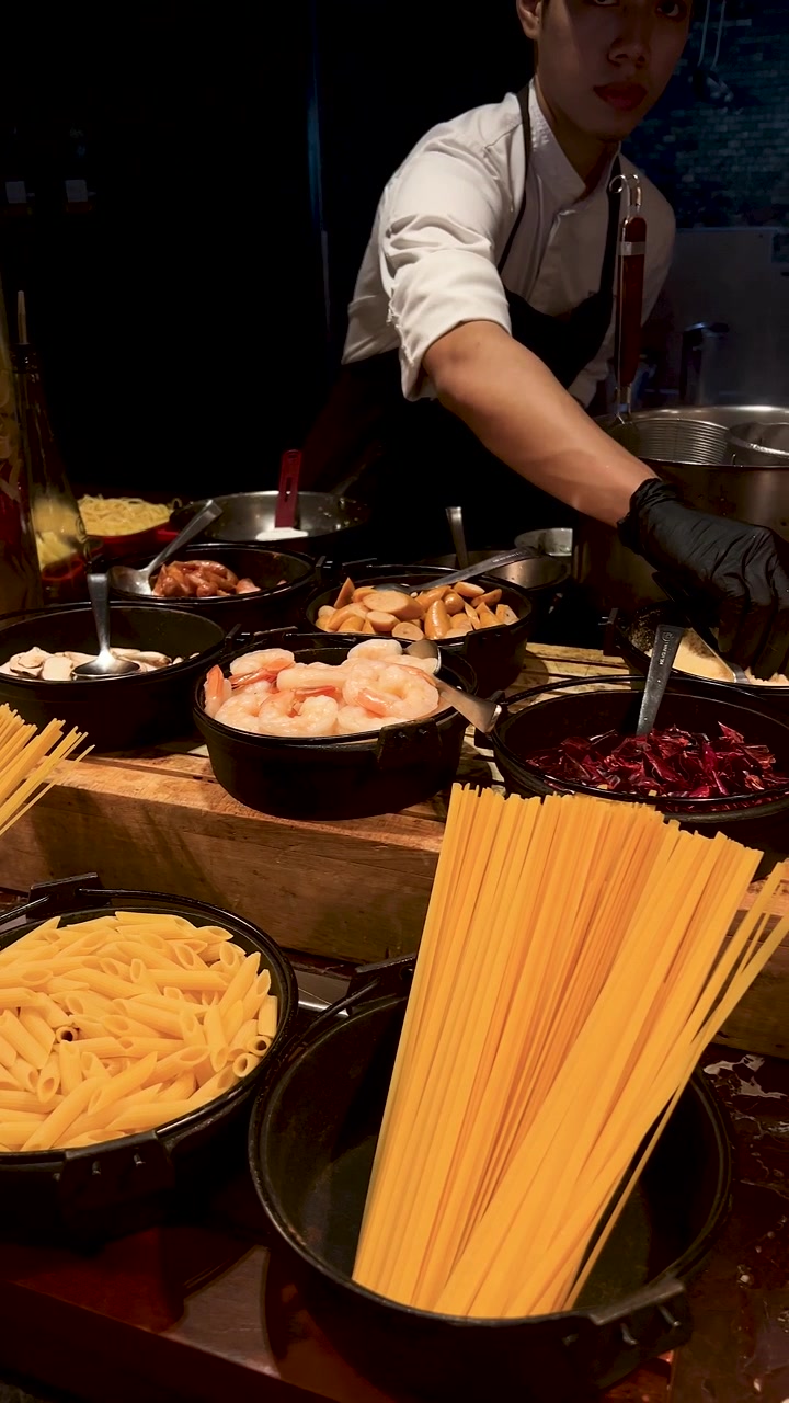 A professional chef in a black apron prepares seafood pasta at a luxury buffet station