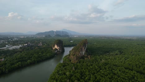 dron aéreo panorámico sobre un bosque de manglares y un río que corre entre dos grandes rocas de montaña de piedra caliza en una tarde de puesta de sol en la ciudad de krabi, tailandia