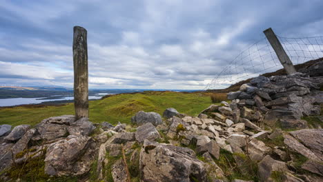 panorama motion timelapse of rural landscape with stonewall, timber pillars and sheep in grass field and hills and lake in distance during cloudy day viewed from carrowkeel in county sligo in ireland