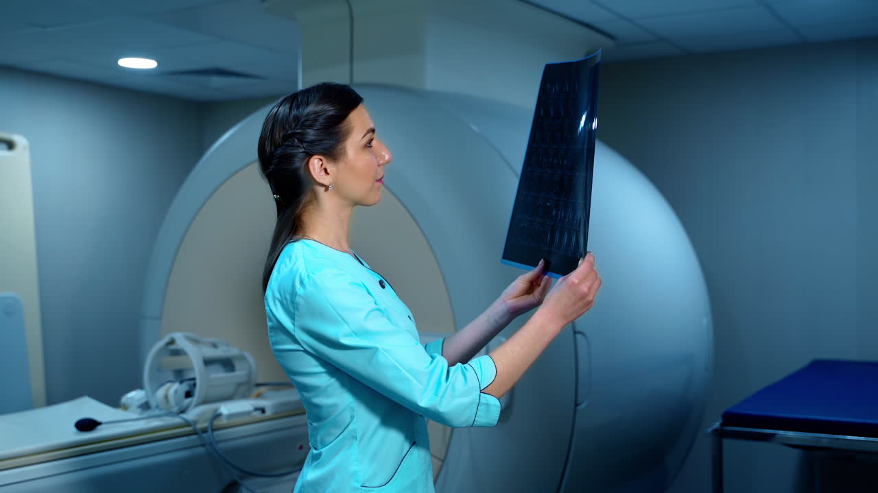 Doctor looks at an x-ray photo of a patient. Female laboratory worker examining x-ray picture on the background of MRI machine.