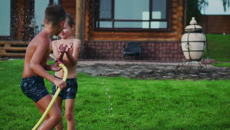 mother with father and two children playing on the lawn pouring water laughing and having fun on the playground with lawn on the background of his house near the lake in slow motion