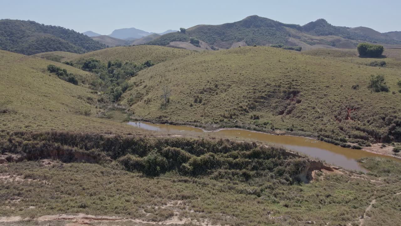 subiendo detrás del pasto en la colina se ve una pequeña laguna con agua fangosa como un pantano escondido con montañas en el horizonte