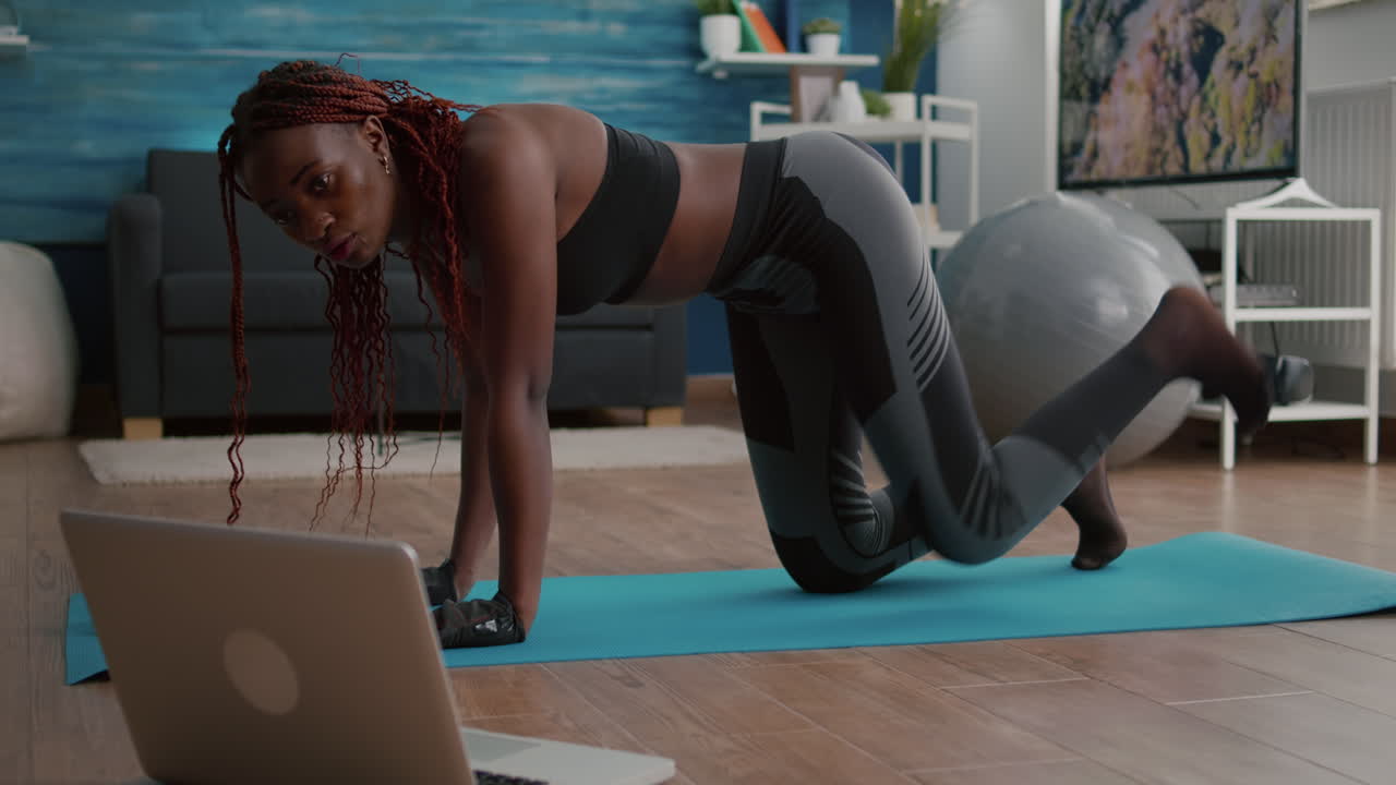 Adult black woman sitting on yoga map watching online fitness workout