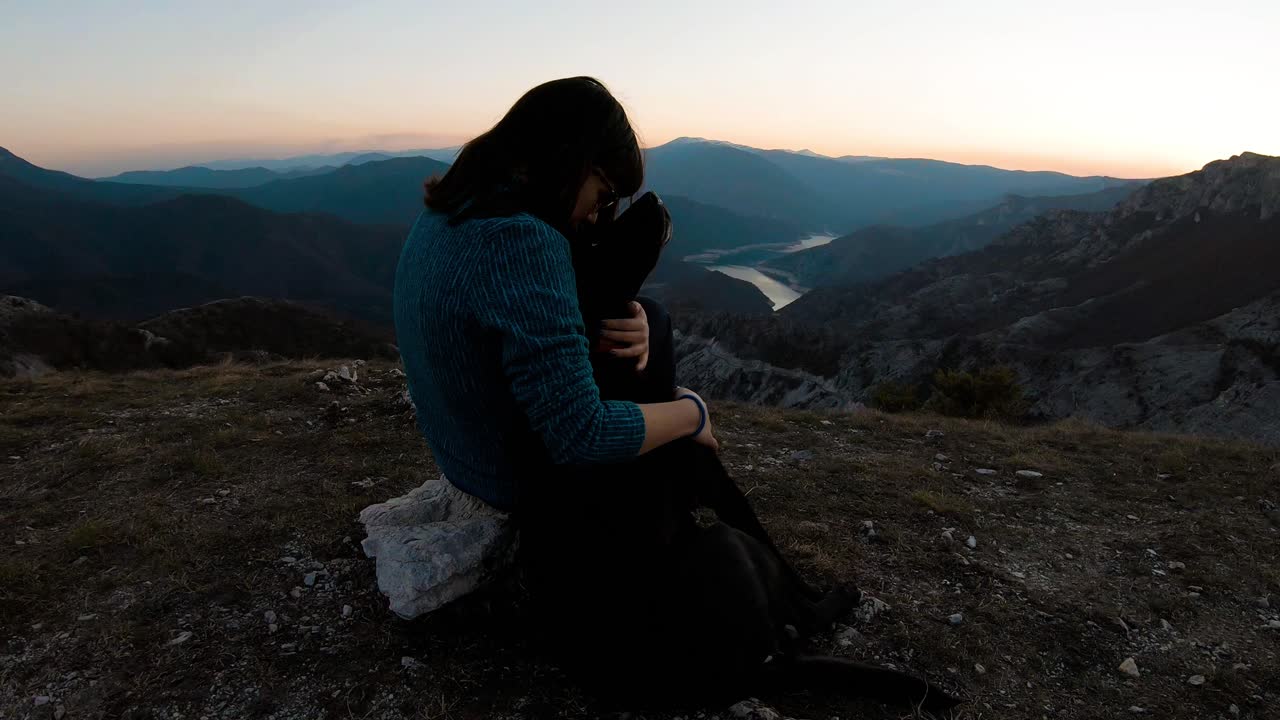 niña abrazando a un perro labrador negro en una montaña.
