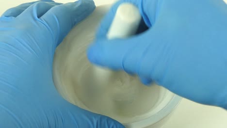 macro shot of a cosmetic laboratory process where gloved hands in blue gloves mix a cream using a porcelain mortar and pestle.