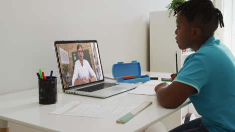 niño afroamericano sentado en un escritorio usando una computadora portátil teniendo una lección escolar en línea