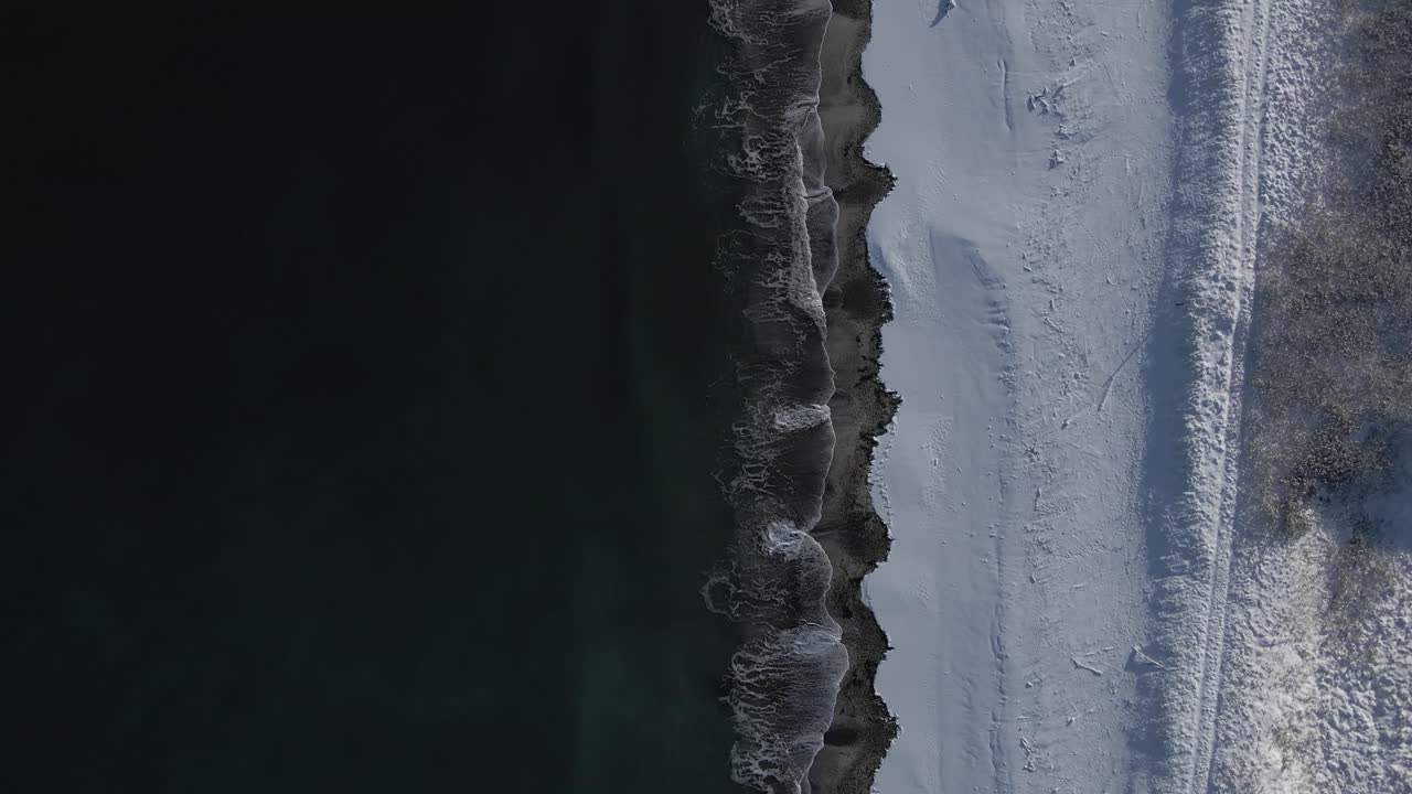 Top down aerial view of snow covered beach and ocean water