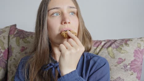 chica joven en el sofá saboreando una deliciosa galleta de chocolate