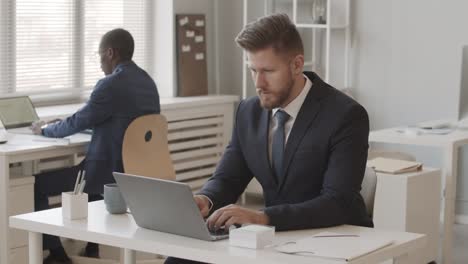 two diverse businessmen working on laptops in office