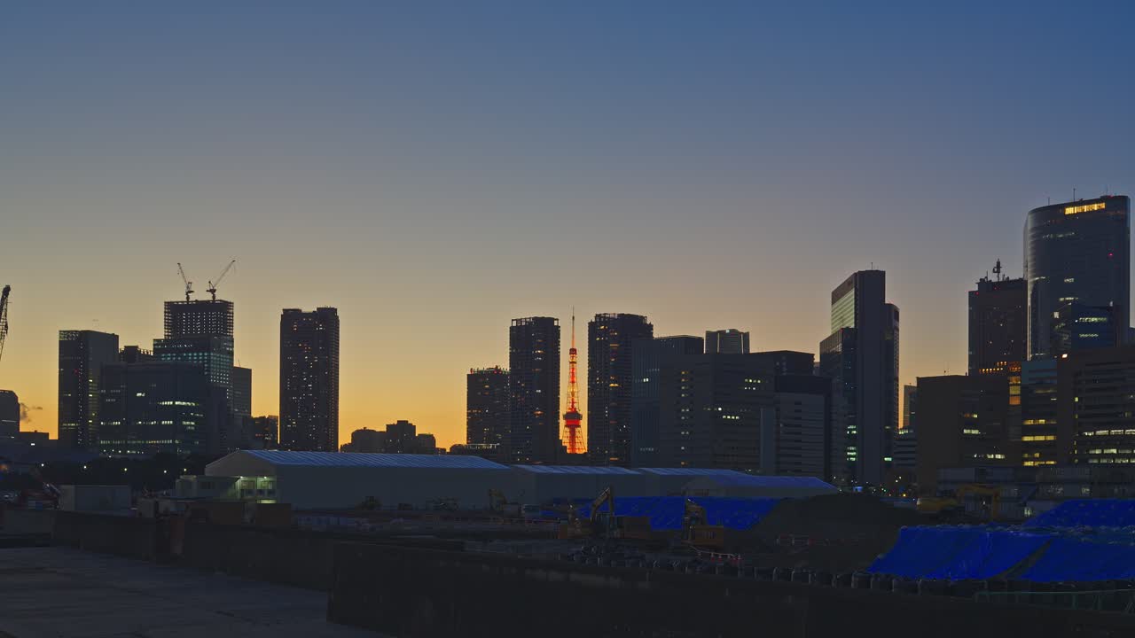 Silueta del horizonte de la ciudad de Tokio al anochecer con rascacielos iluminados, una torre de comunicaciones roja resplandeciendo en el centro y un cielo con un degradado cálido de naranja a azul, capturada como una toma amplia estática.