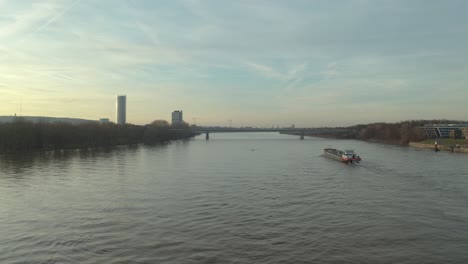 Cinematic drone - aerial shot of a ship on the river rhine in bonn with the post tower the Kameha Grand Hotel and the konrad-adenauer bridge at the golden hour, 25p