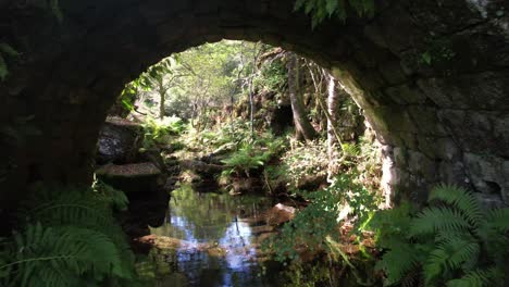 Volando-Sobre-El-Antiguo-Puente-De-Piedra-Sobre-El-Hermoso-Río