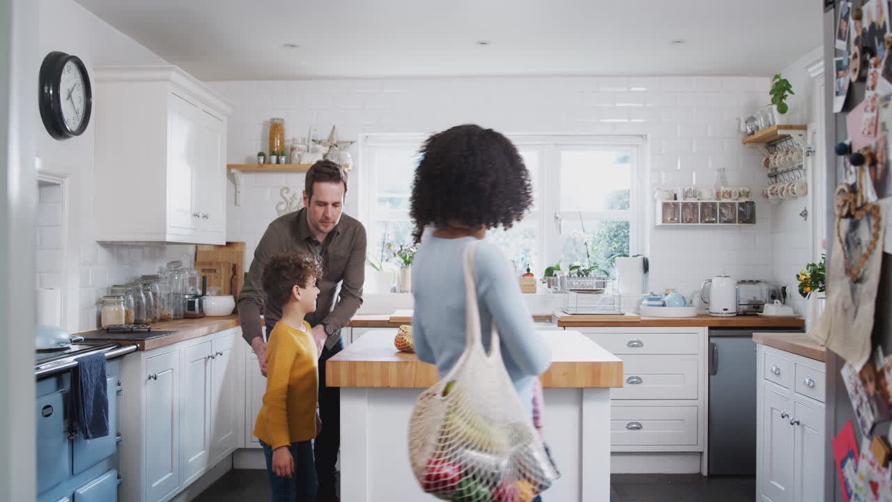 Family Returning Home From Shopping Trip Using Plastic Free Bags Unpacking Groceries In Kitchen