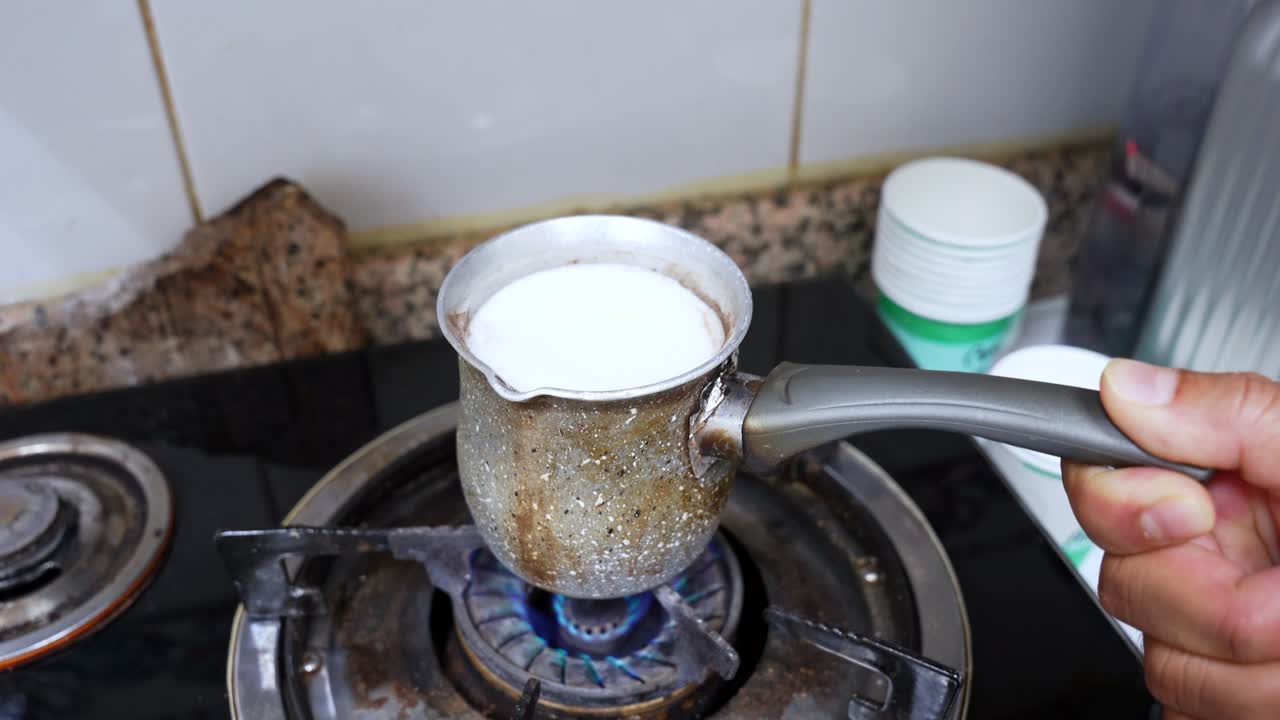 Hot milk bubbling with foam in a rustic metal pot over gas flame. Great for food prep, traditional kitchen scenes, recipe intros, and cultural or home cooking visuals.