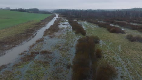 aerial establishing view of high water in springtime, alande river flood, brown and muddy water, agricultural fields under the water, overcast day, wide drone dolly shot moving right low