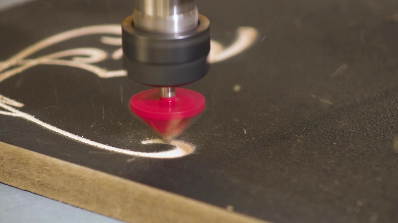 Macchina fresatrice CNC che incide su una piastra nera di legno MDF con una punta da trapano, al rallentatore.