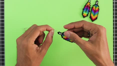 hands crafting colorful bead earrings on green background, creative hobby concept, top view