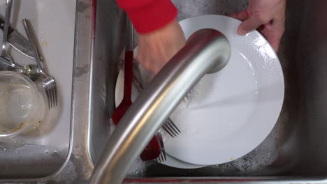 top down view, faucet running, cleaning dirty plates and spatula in sink with with palm dish brush