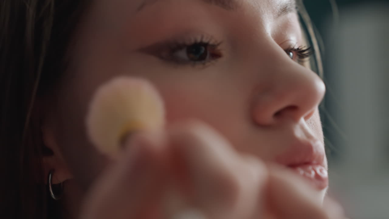 Closeup caucasian woman applying blush brush, soft natural makeup, dewy skin, slow deliberate strokes, mirror and vanity in morning light, model practicing subtle editorial look, gentle selfcare mood