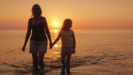 An-Attractive-Mother-Walks-With-Her-Daughter-On-The-Water-Against-The-Backdrop-Of-The-Setting-Sun-A-