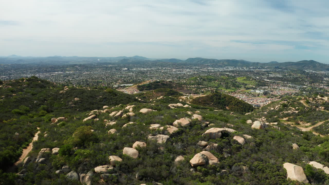 Flying over open space with boulders and chaparral towards developments in Escondido, CA