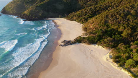 Hochkippende-Drohnenaufnahme-Des-Rauchigen-Nordstrandes-Mit-Dem-Rauchigen-Kap-Leuchtturm-Im-Hintergrund-In-Australien