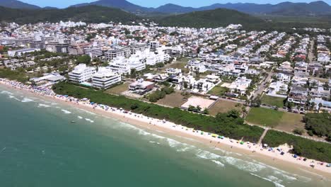 escena de altitud de drones aéreos de playa turística con muchos alojamientos frente al mar, edificios de vuelo y casas con gente divirtiéndose en la playa en florinópolis jurere internacional